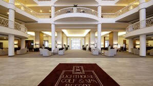 Un vestíbulo espacioso con una zona de estar central, varios niveles con barandillas ornamentales y un letrero destacado que dice "Lighthouse Golf & Spa Resort".