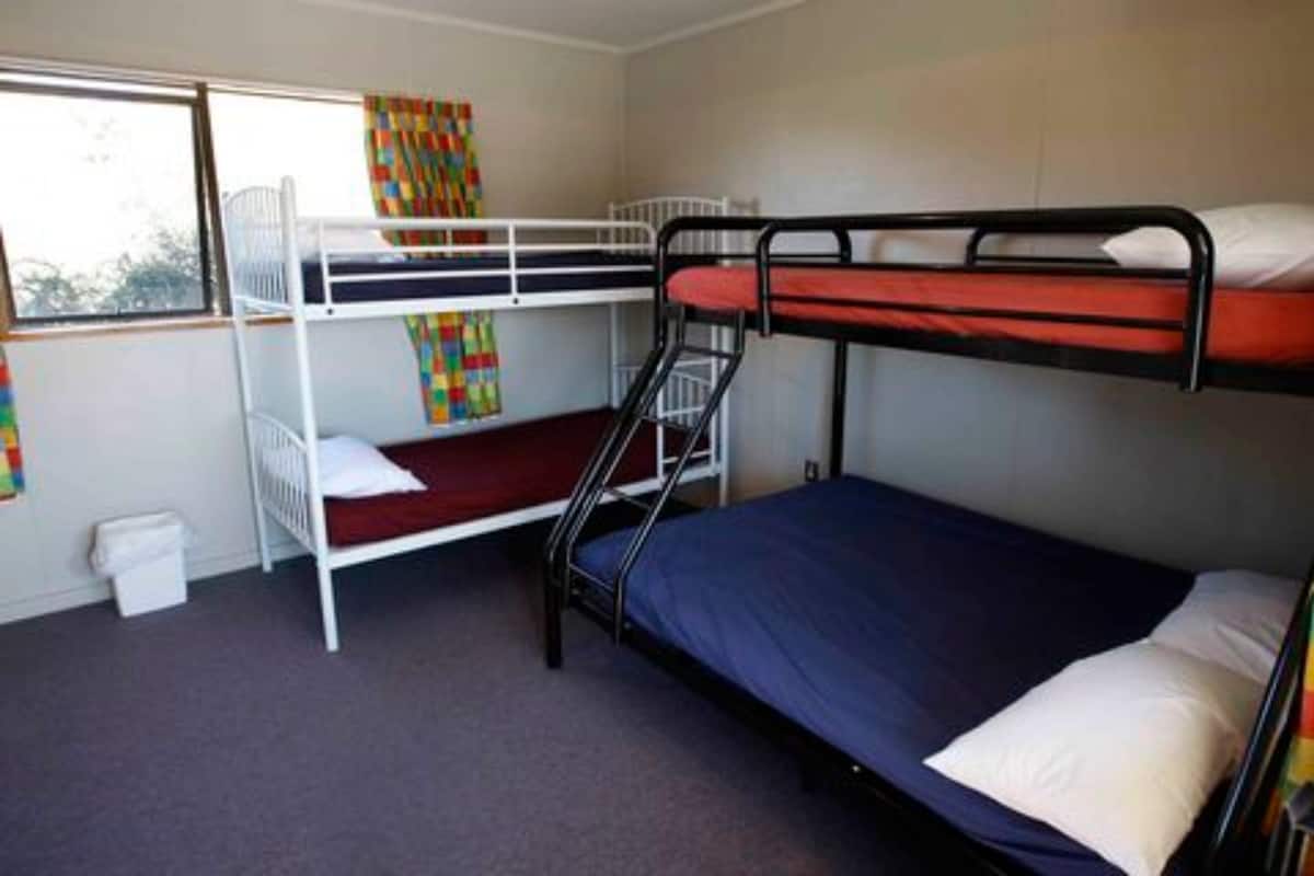 A bunk bed room with a window, a small trash bin, and a colorful curtain.