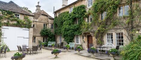 A courtyard with stone buildings, outdoor seating, and potted plants.