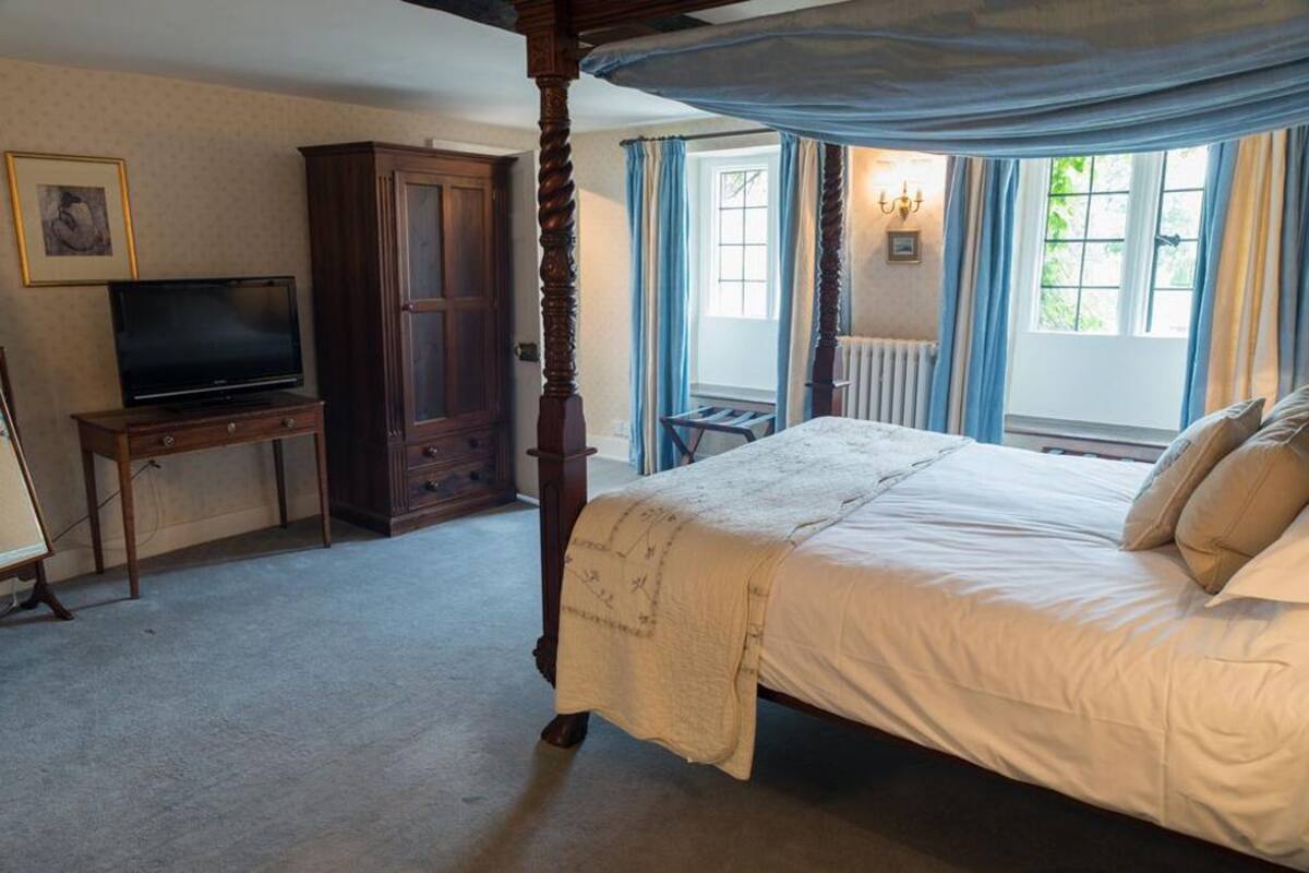 Un dormitorio con una cama con dosel, un televisor sobre un mueble de madera y una ventana con cortinas.
