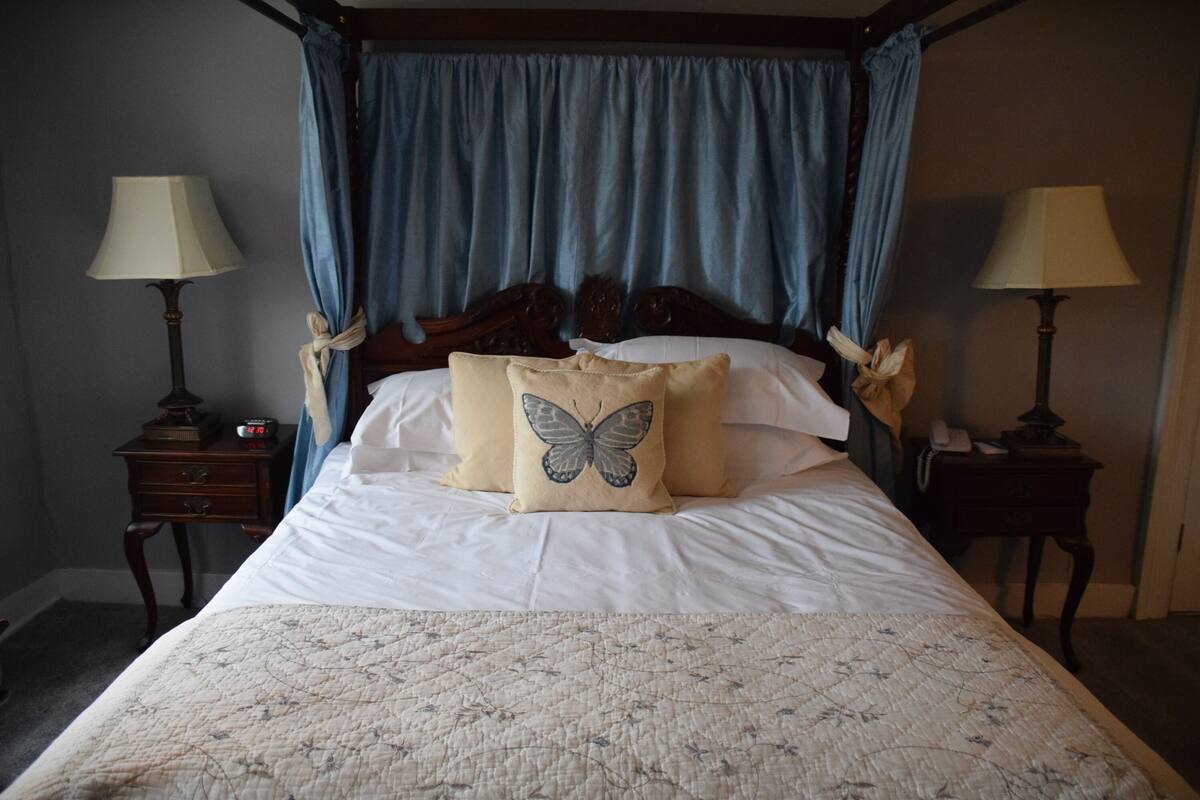 Una cama con dosel y cortinas, dos mesitas de noche con lámparas y una colcha con estampado floral.