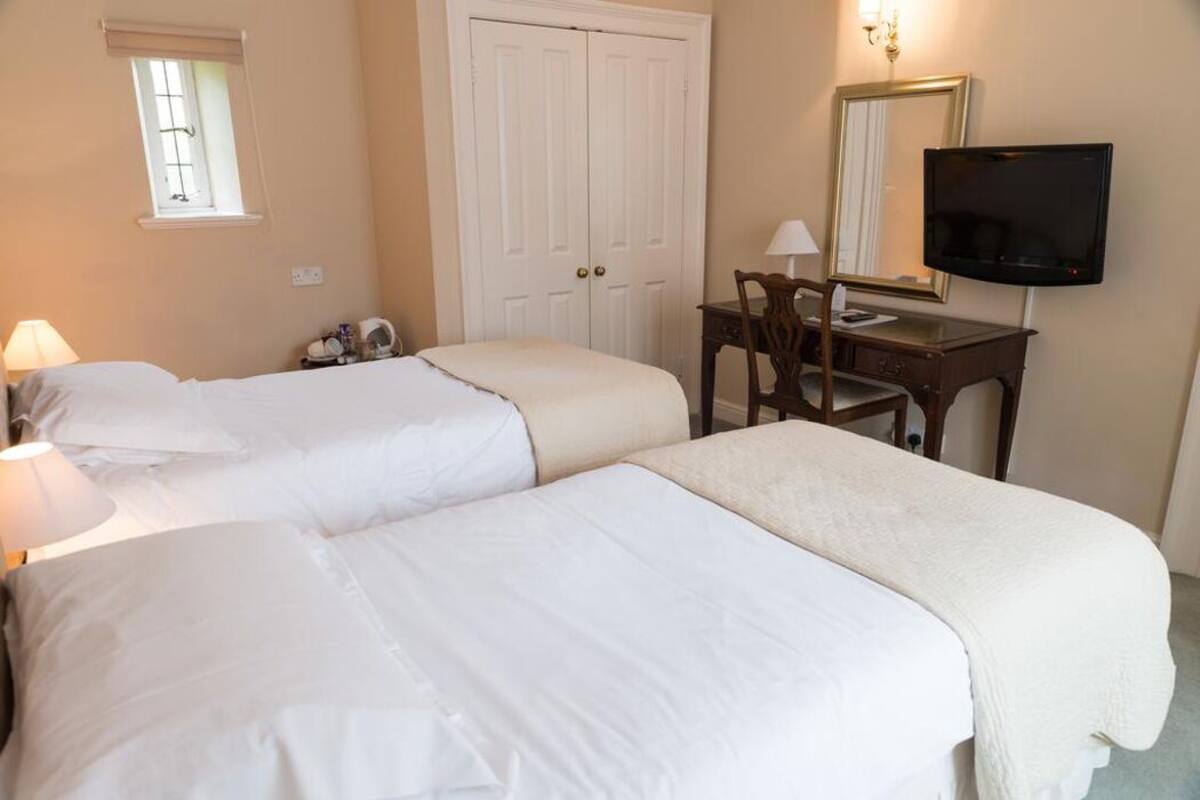 Una habitación de hotel con dos camas, un escritorio con silla, un televisor y un armario.