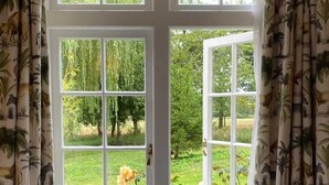 Una ventana con vista a un jardín, cortinas con estampado tropical y un tirador de latón.