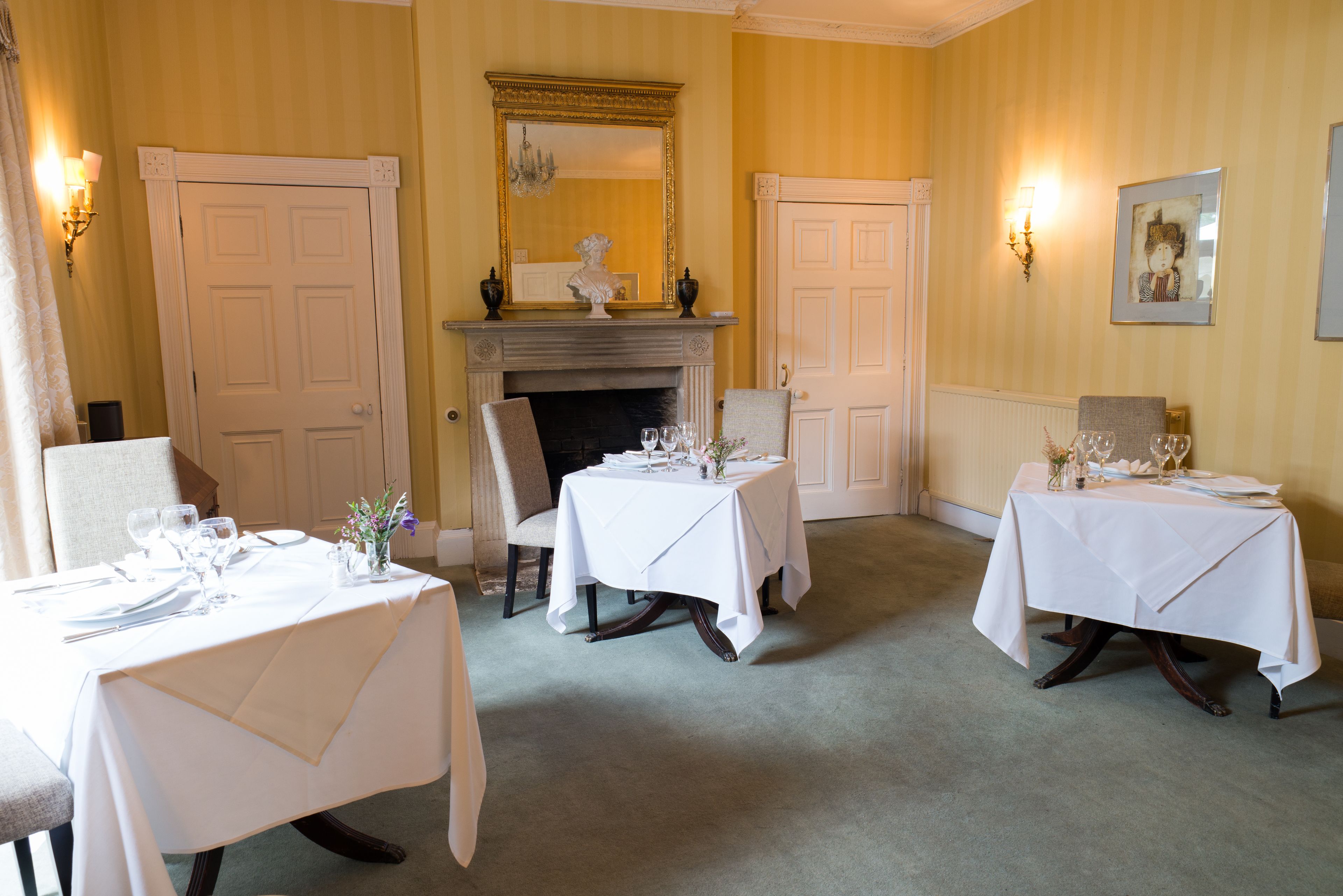 A dining room with three tables set for a meal, a fireplace, and a mirror above the mantel.