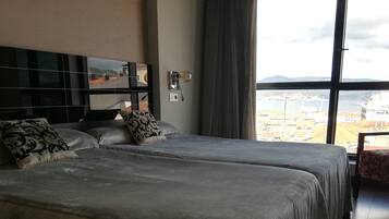 Habitación de hotel con dos camas, un ventanal con vistas a la ciudad, un espejo y una silla.