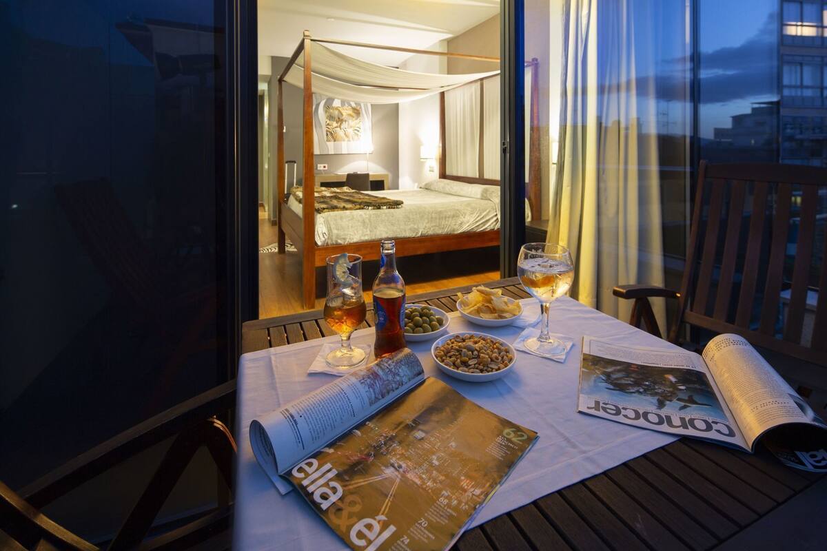A balcony with a table set for dining, a magazine, and a bottle of beer.