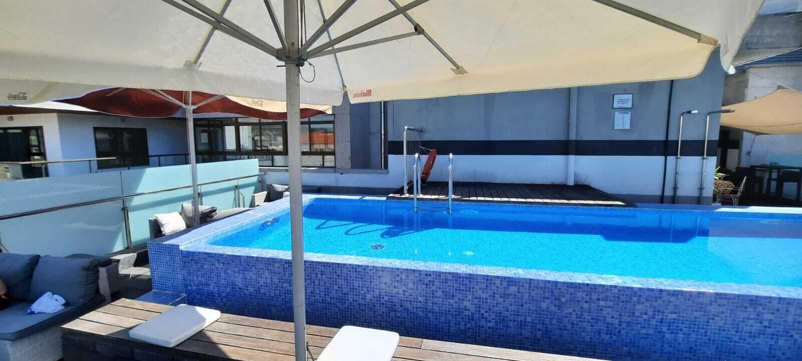 Una piscina en la azotea con sillones de descanso y sombrillas.