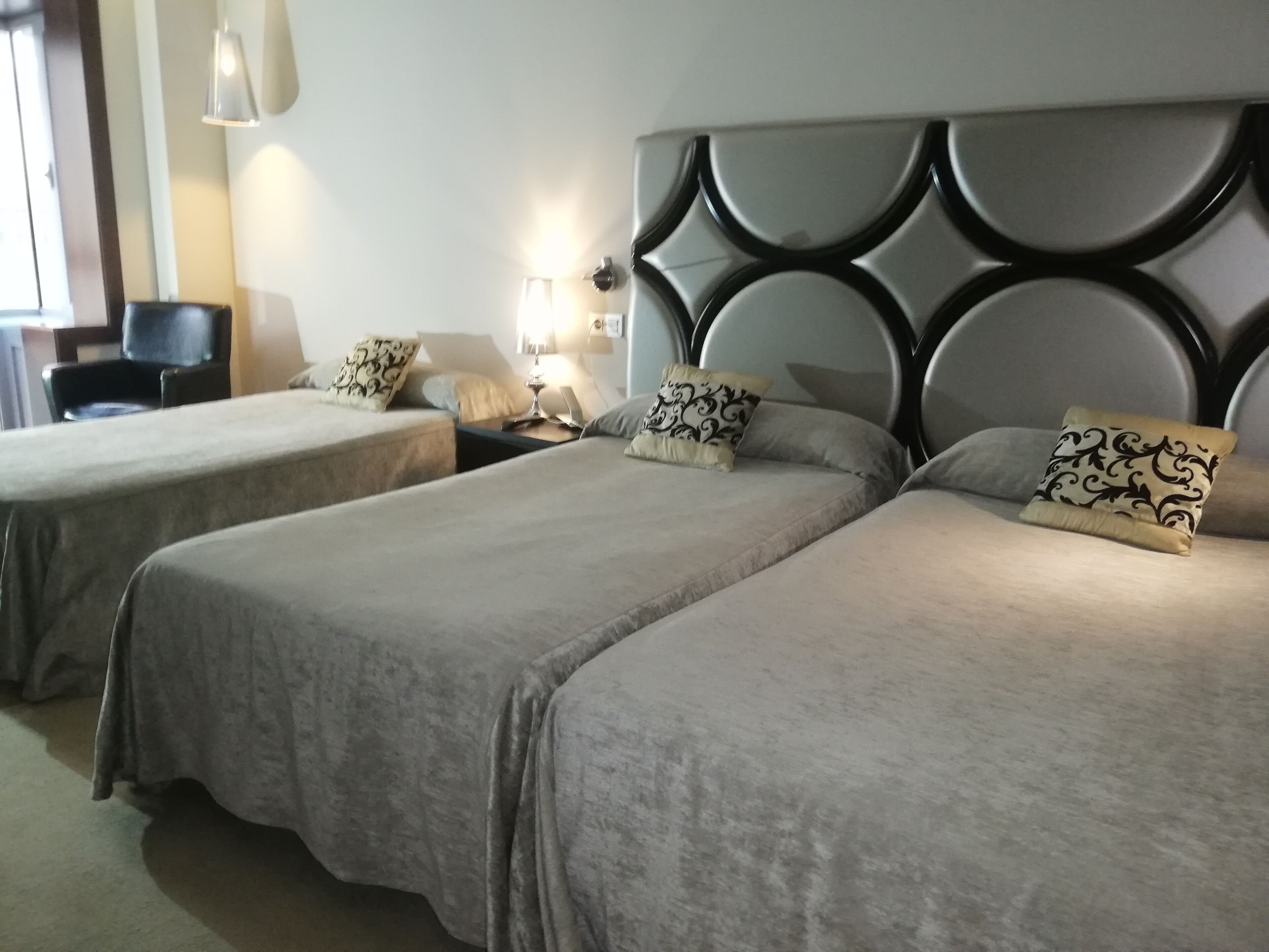 Una habitación de hotel con dos camas individuales, una mesita de noche con lámpara y una silla.