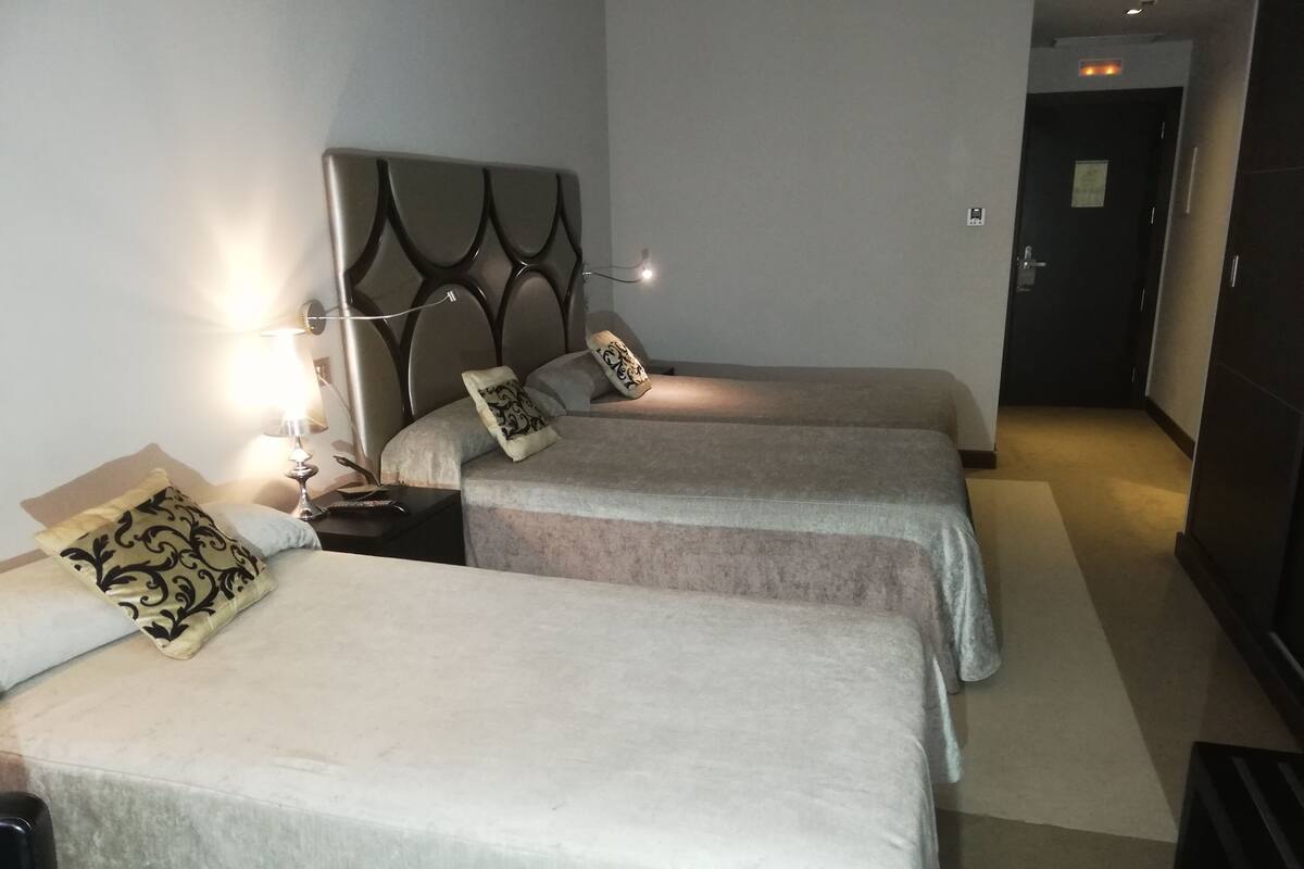 A hotel room with two beds, a nightstand with a lamp, and a door leading to another room.