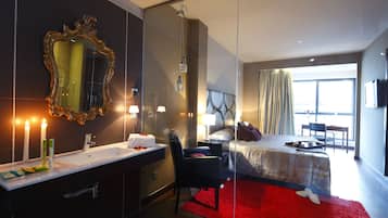 Una habitación de hotel moderna con un espejo grande, una cama con alfombra roja, un escritorio y vistas al exterior.