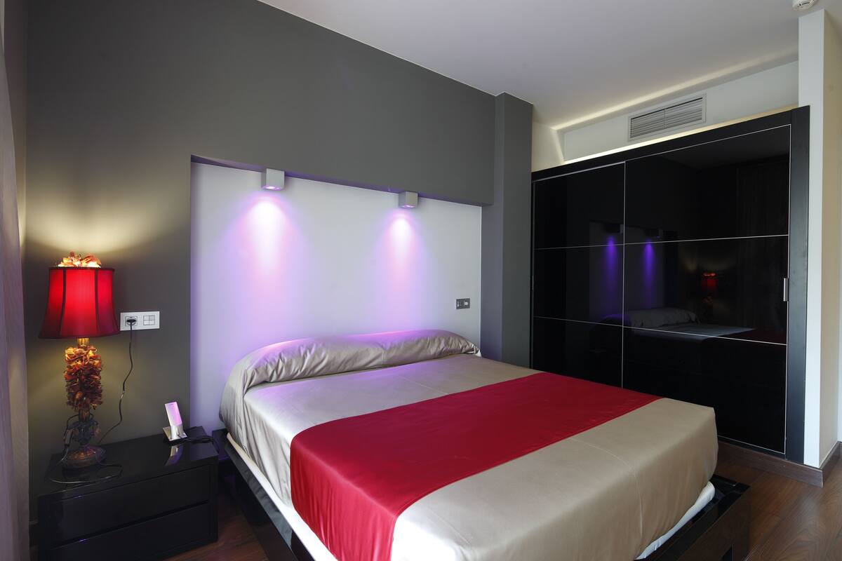 A modern bedroom with a bed, bedside table, lamp, and a wardrobe.