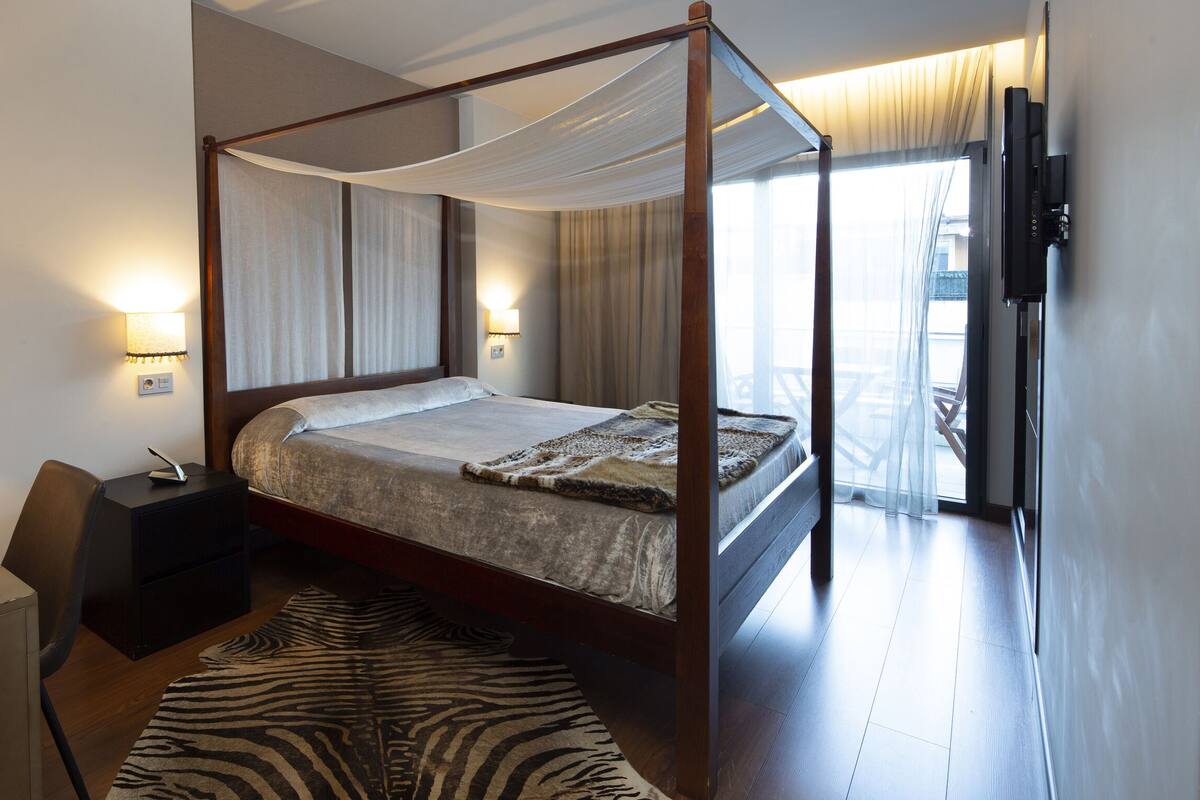 A four-poster bed with a canopy, a desk with a lamp, and a zebra-patterned rug.