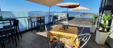 A terrace with outdoor seating, a table with a yellow checkered tablecloth, and potted plants.