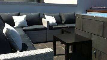 A sunlit outdoor seating area with a sofa and a table, a tiled floor, and a blue wall.