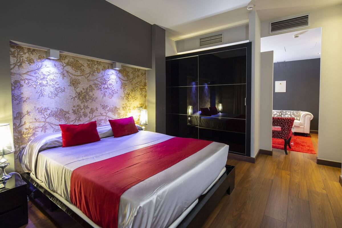 A modern hotel room with a large bed, a wardrobe, a TV, and a small seating area.