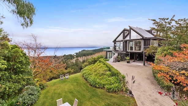 Una casa grande con vista al mar, rodeada de un jardín cuidado y un camino pavimentado.