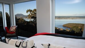 Un dormitorio con un amplio ventanal que ofrece vistas a un lago y montañas distantes.