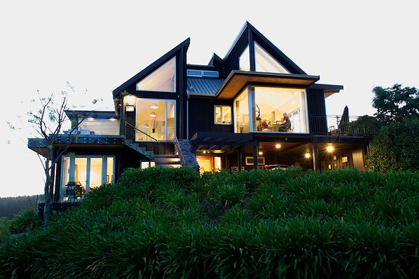 A modern two-story house with large windows and a balcony, surrounded by lush greenery. - Acacia Cliffs Lodge (Taupo)