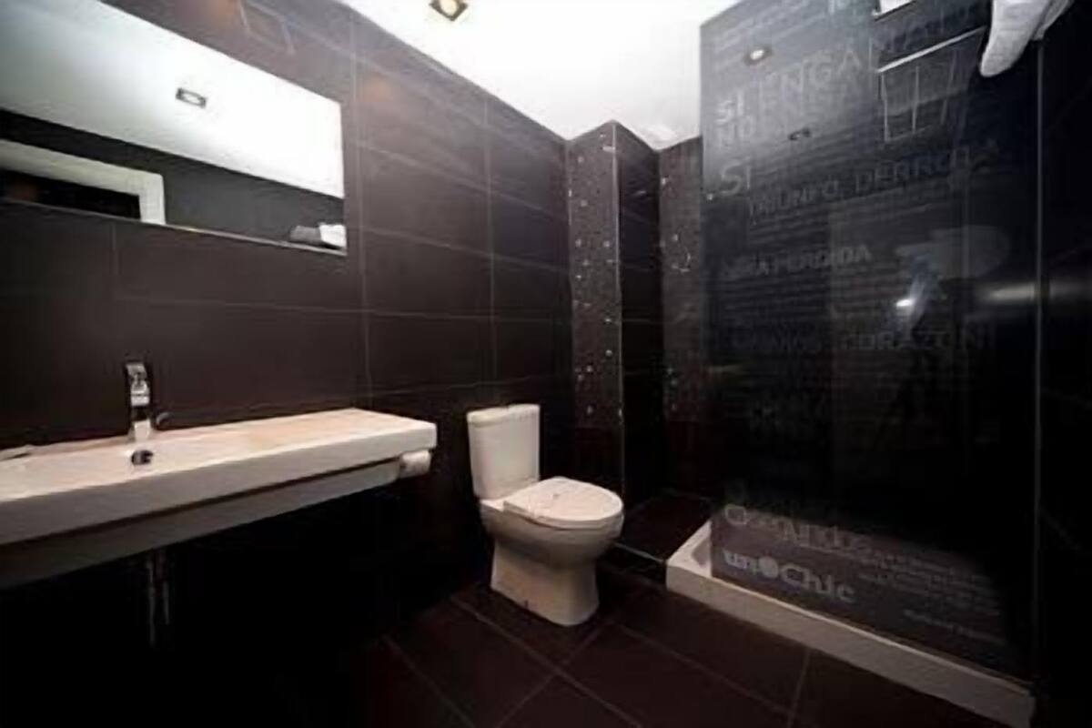 Une salle de bain moderne avec un mur recouvert de carreaux foncés, un lavabo blanc et une cabine de douche en verre.