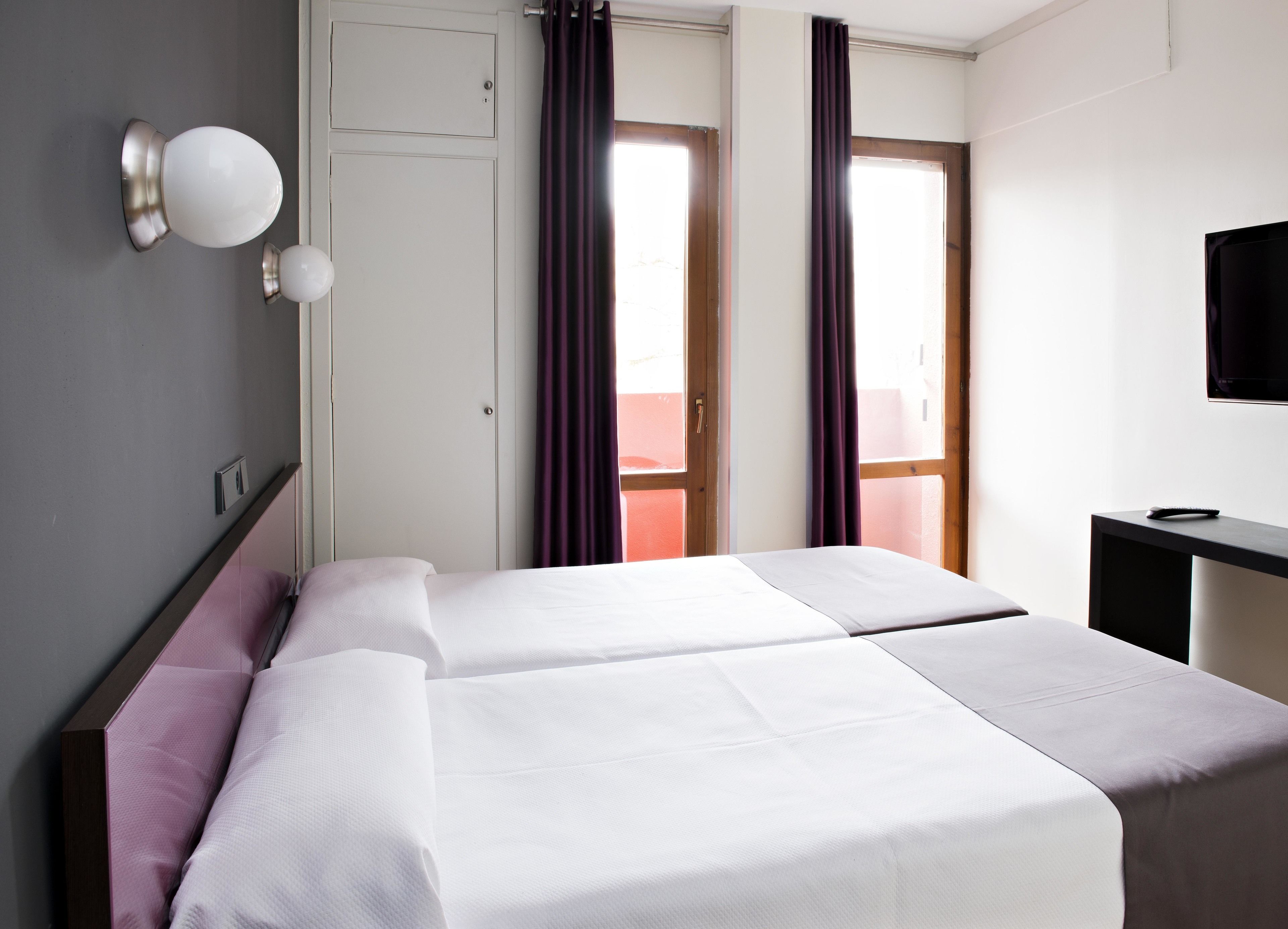 A hotel room with two beds, a desk, a TV, and a window with curtains.
