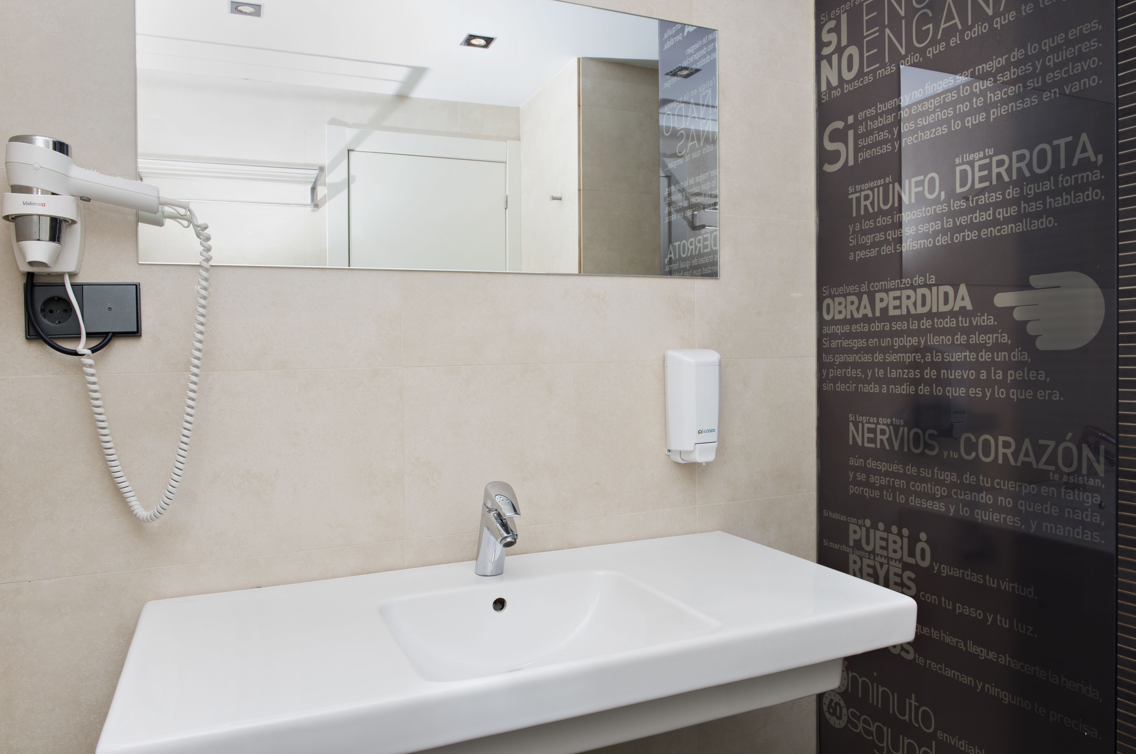 A bathroom with a white sink, a hairdryer, and a mirror.