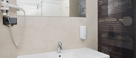 Casa de banho com lavatório branco, secador de cabelo e espelho.