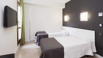 Habitación de hotel con dos camas, televisión y ventana con cortina verde.