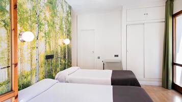 A hotel room with two beds, a large window with curtains, a wardrobe, and a wall with a nature-themed wallpaper.