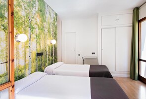 Habitación de hotel con dos camas, un ventanal con cortinas, un armario y una pared con papel tapiz de motivos naturales.