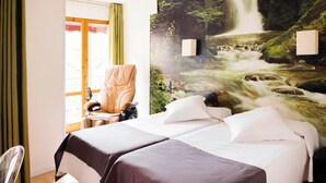 Habitación de hotel con cama, una silla, escritorio y un gran mural en la pared con una cascada.