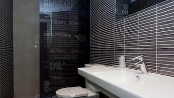 Un baño moderno con un lavamanos blanco, un grifo cromado y un inodoro. Las paredes están decoradas con letras grandes y oscuras en español.