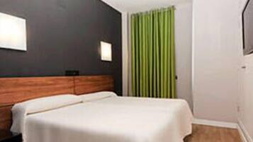 A hotel room with a bed, a wooden headboard, a green curtain, and a white wall with a light fixture.