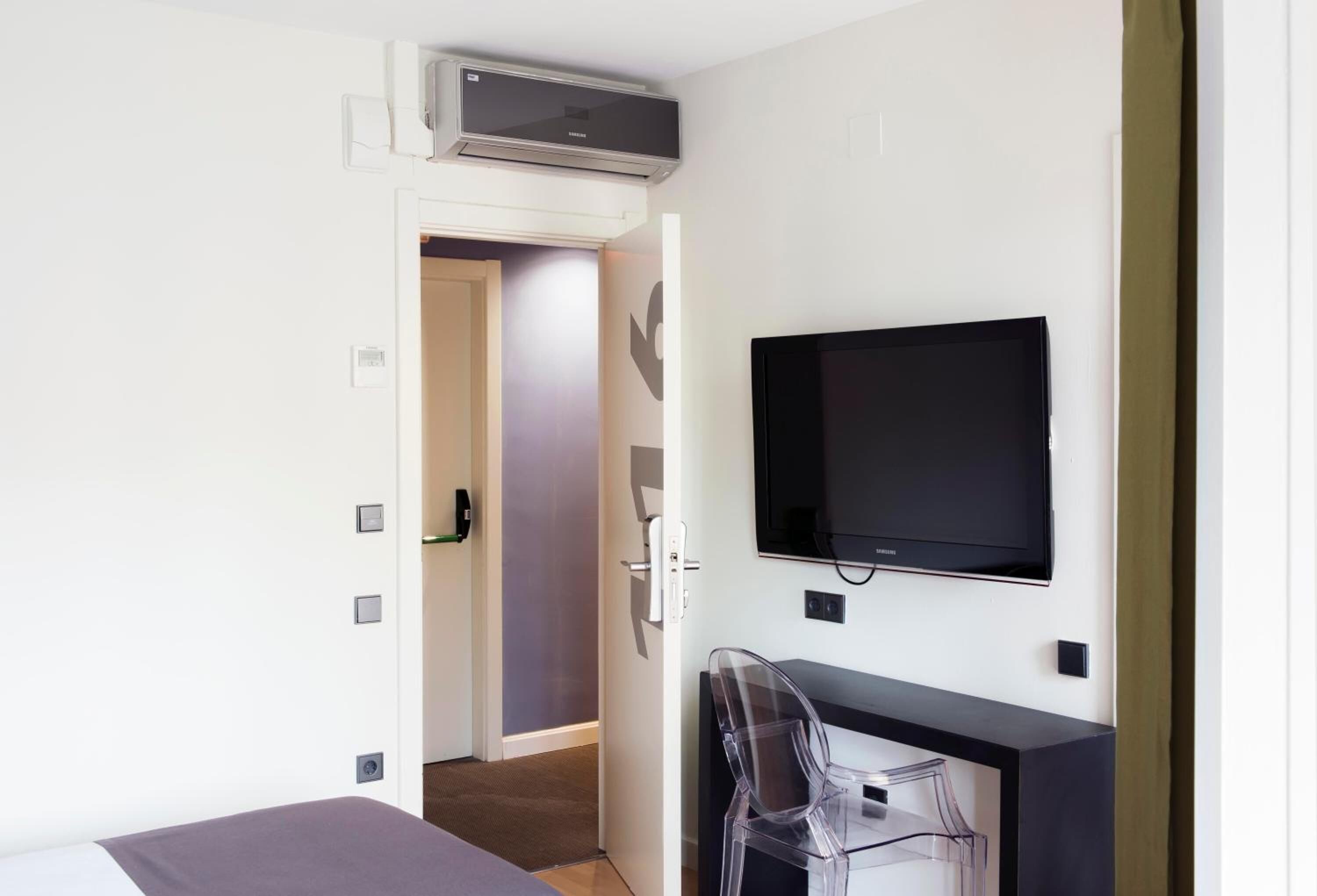 Een hotelkamer met een bed, een bureau met stoel, een wandtelevisie en een airconditioning.