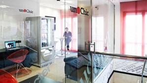 Un interior moderno con divisiones de vidrio, una computadora portátil sobre un escritorio y una zona de estar con una silla roja.