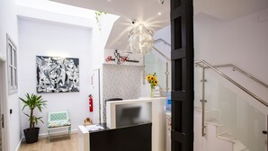 A reception area with a reception desk, a potted plant, a bench, a wall-mounted artwork, and a staircase. - Hostal San Francisco (Seville)