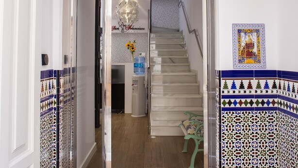 A modern hotel lobby with a staircase, a reception desk, and decorative tiles. - Hostal San Francisco (Seville)