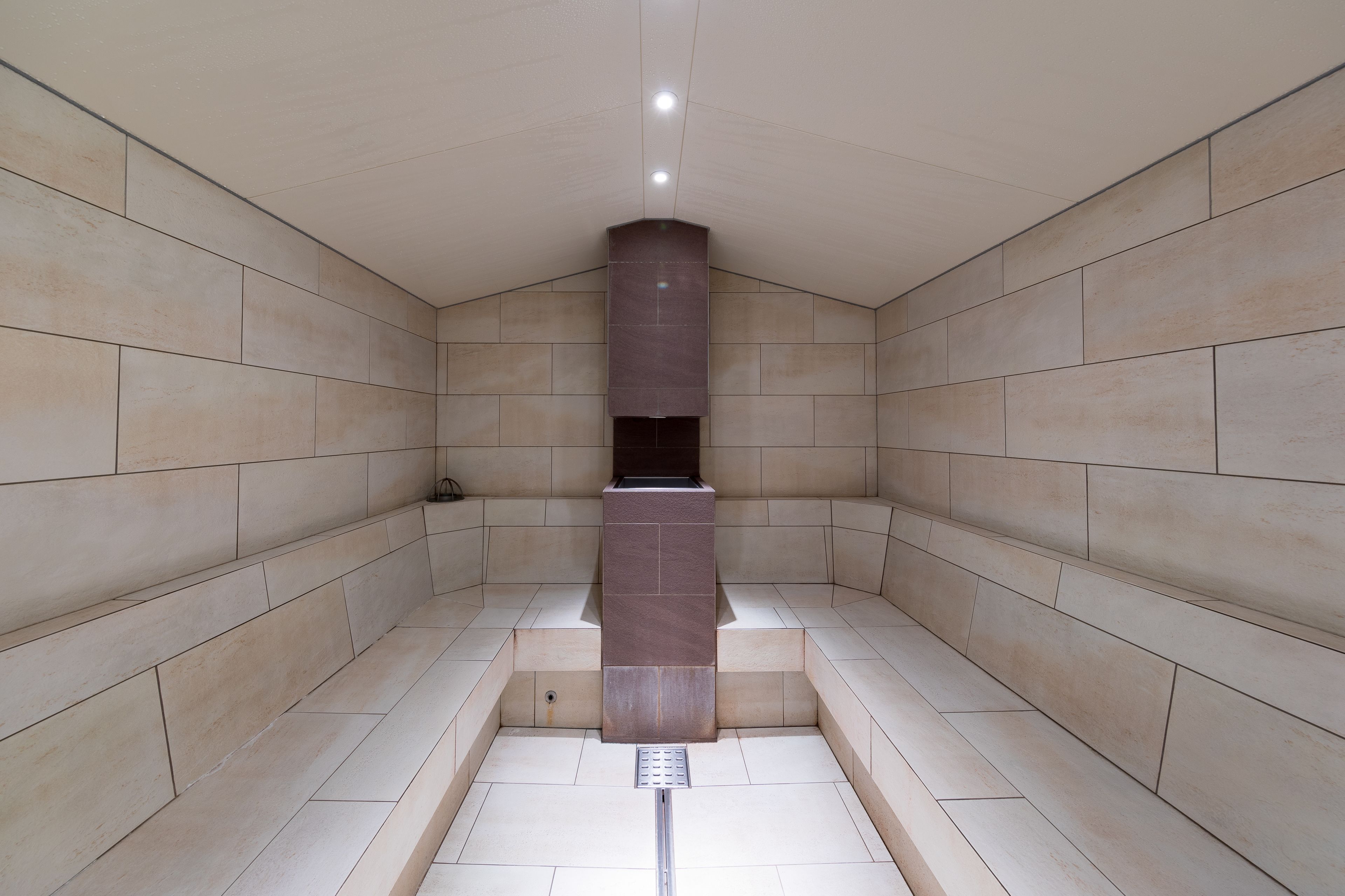 Un baño moderno con un lavamanos central, paredes alicatadas y una lámpara en el techo.