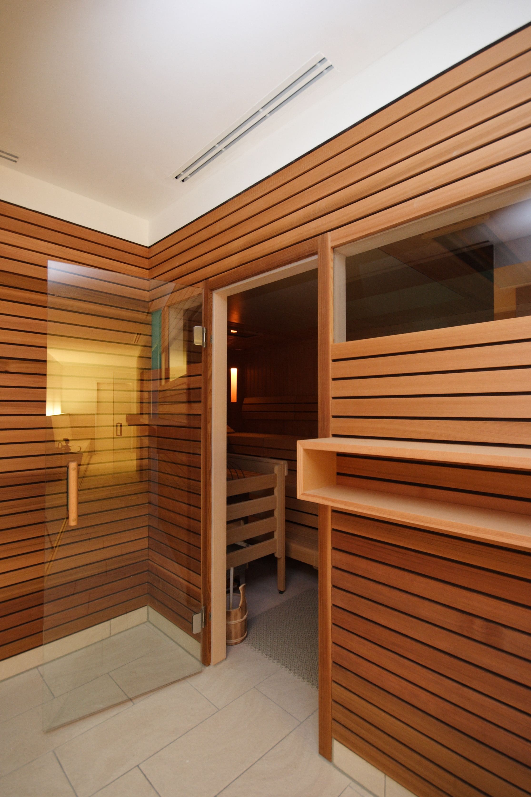 Un sauna moderne avec des panneaux de bois, une porte en verre et un banc.