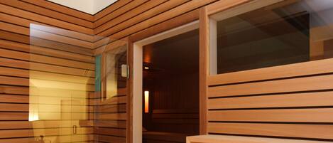 A modern sauna room with wooden paneling, a glass door, and a bench.