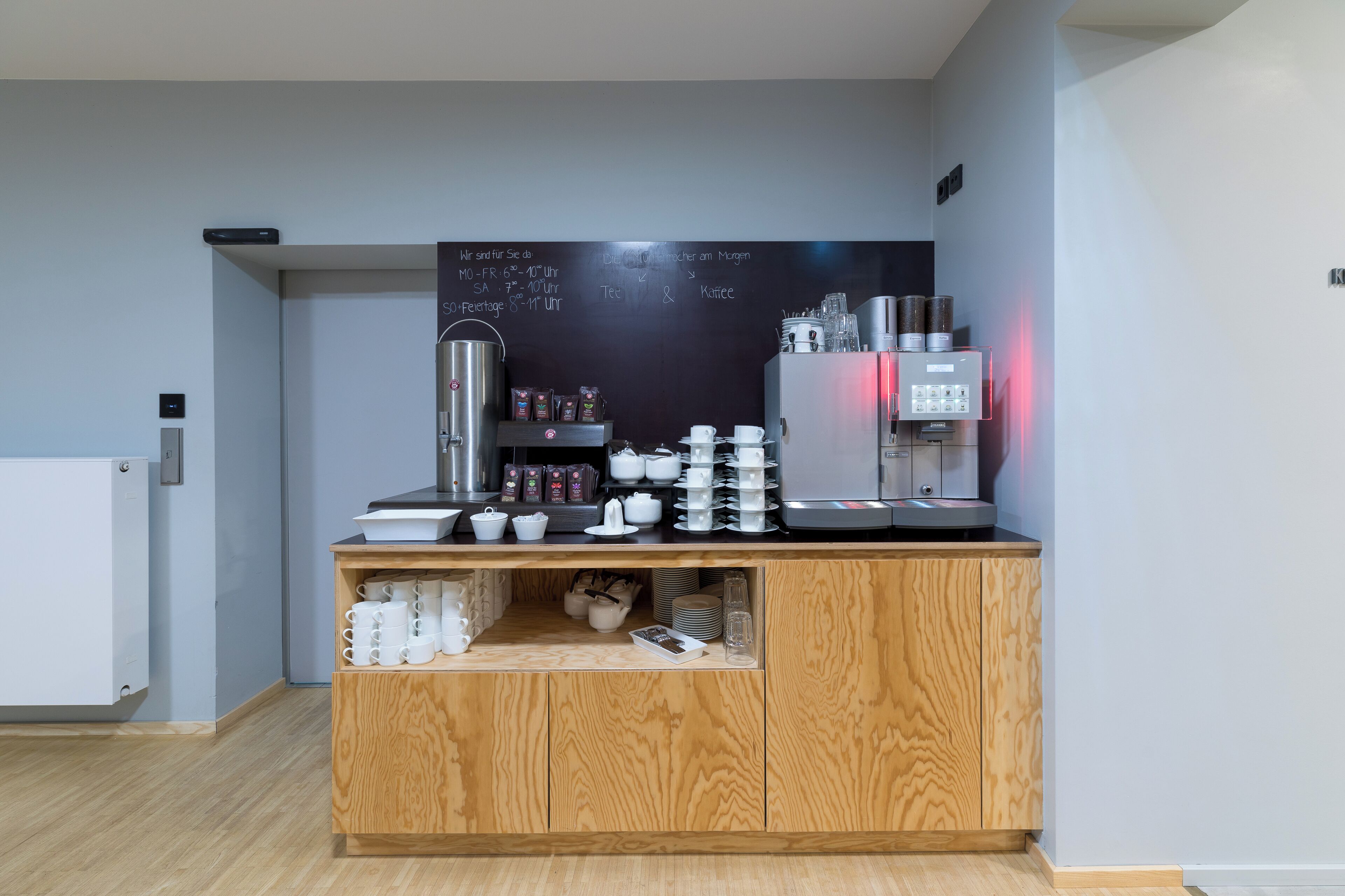 A coffee station with a chalkboard menu, coffee machines, and various coffee cups and mugs.