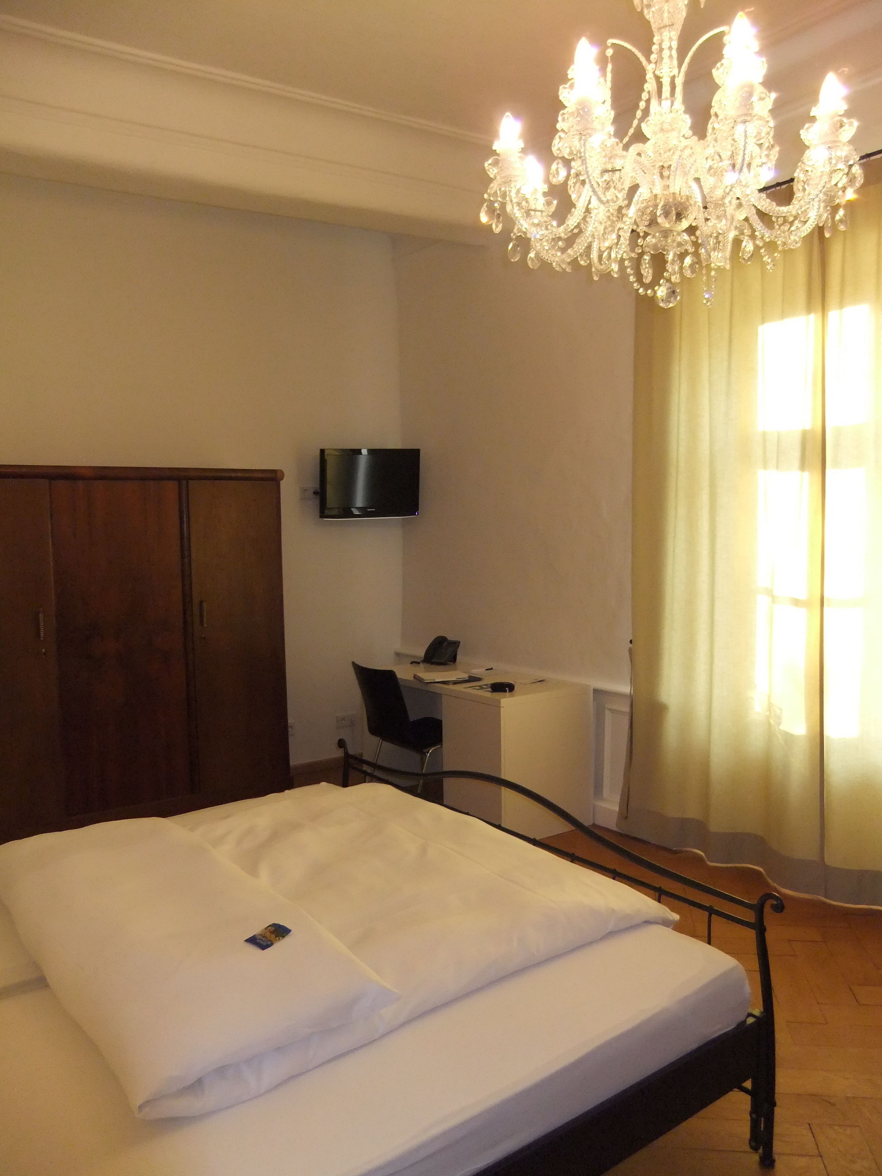 Un dormitorio con cama, escritorio, silla, televisor y candelabro.
