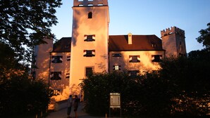 A castle-like building with a prominent tower, a gated entrance, and a signboard.
