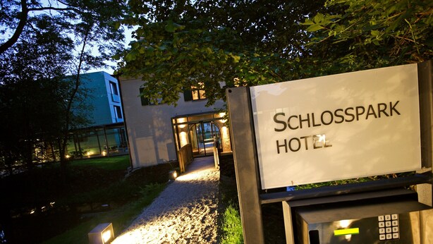 A sign for the Schlosspark Hotel with a pathway leading to the entrance.