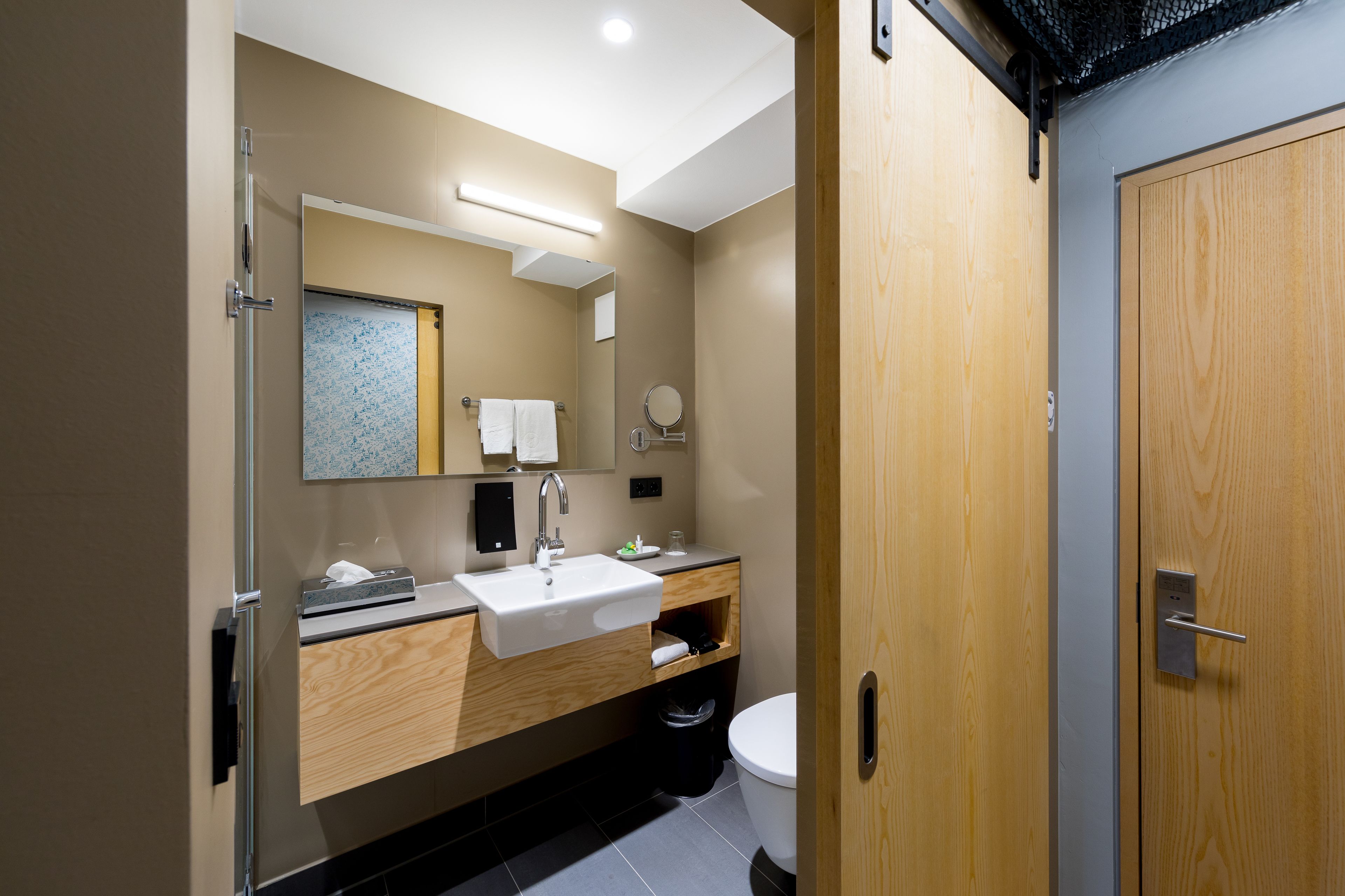 A modern bathroom with a wooden vanity, a white sink, and a toilet.