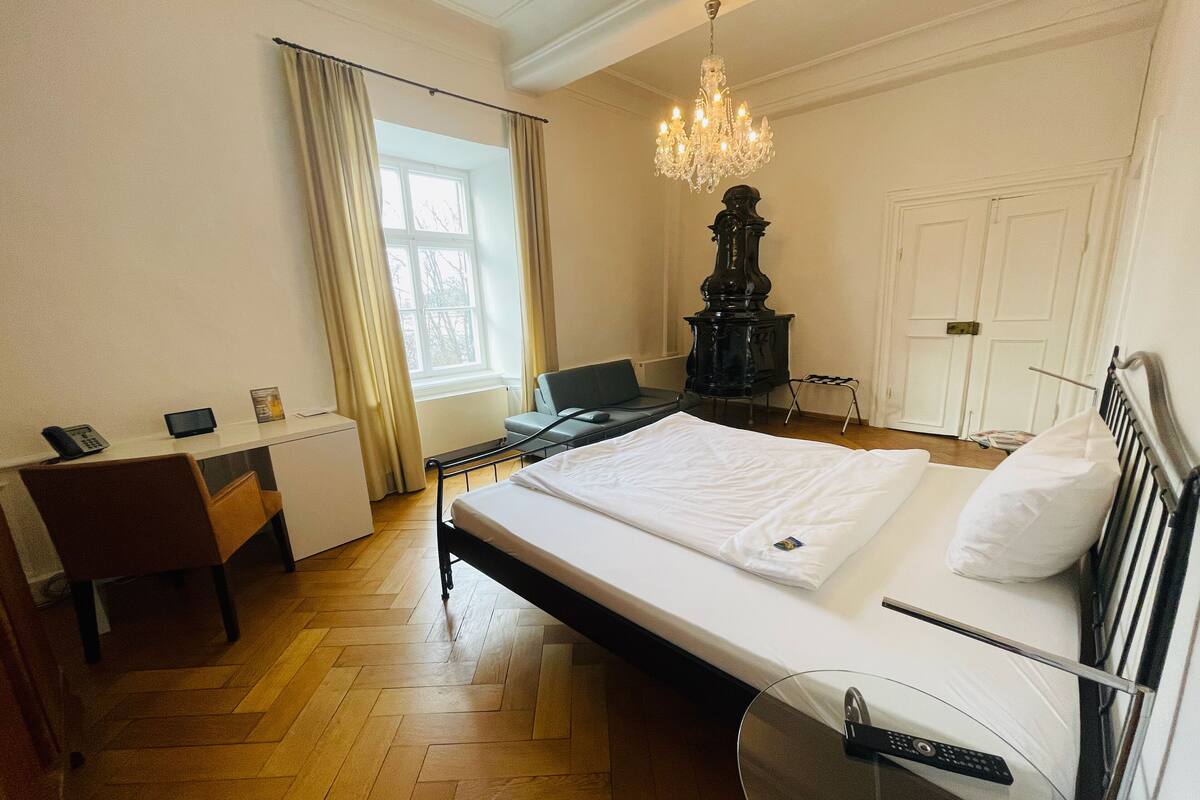 A hotel room with a bed, desk, chair, and a large window.