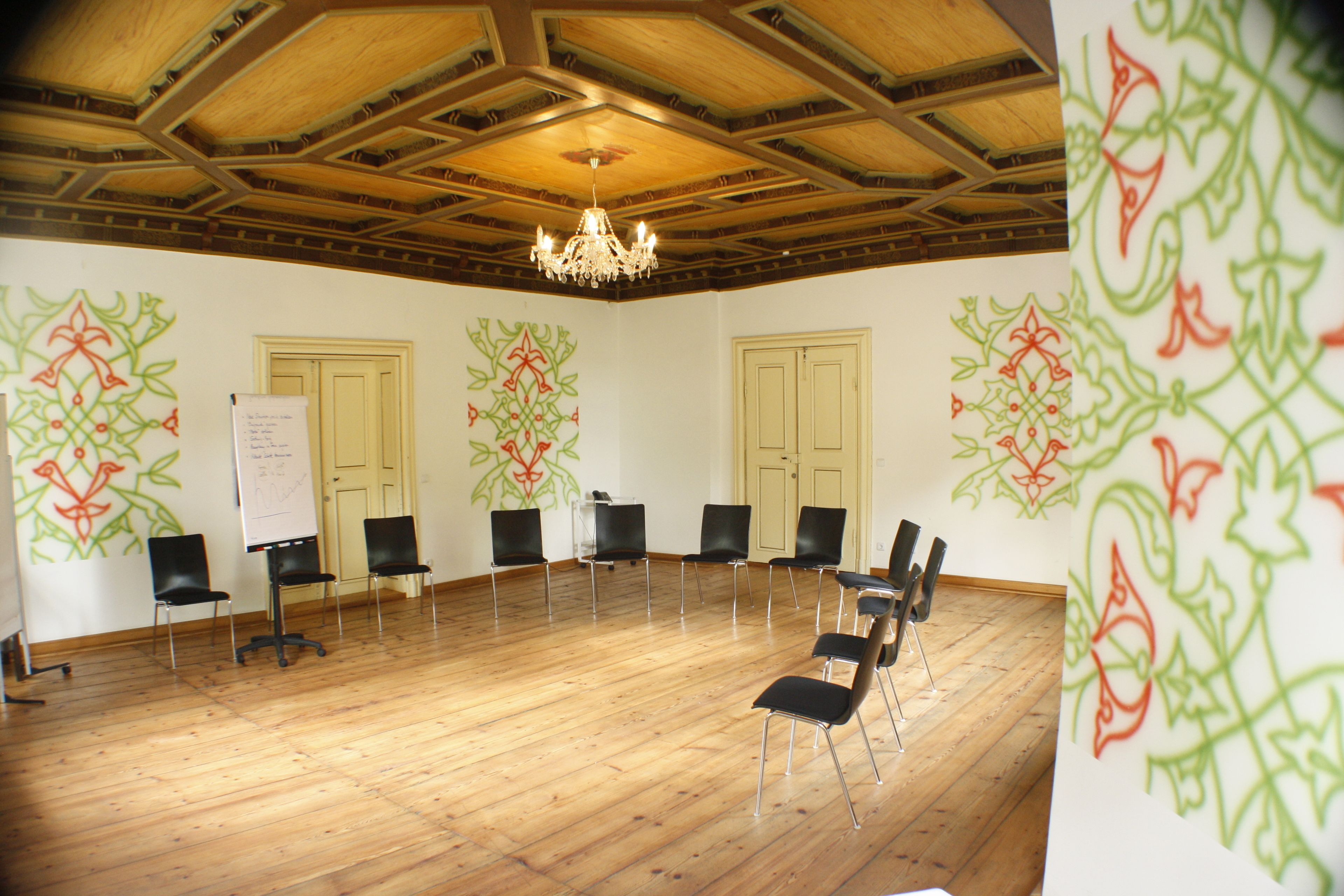 Un salón de conferencias con pisos de madera, una araña y una pizarra.