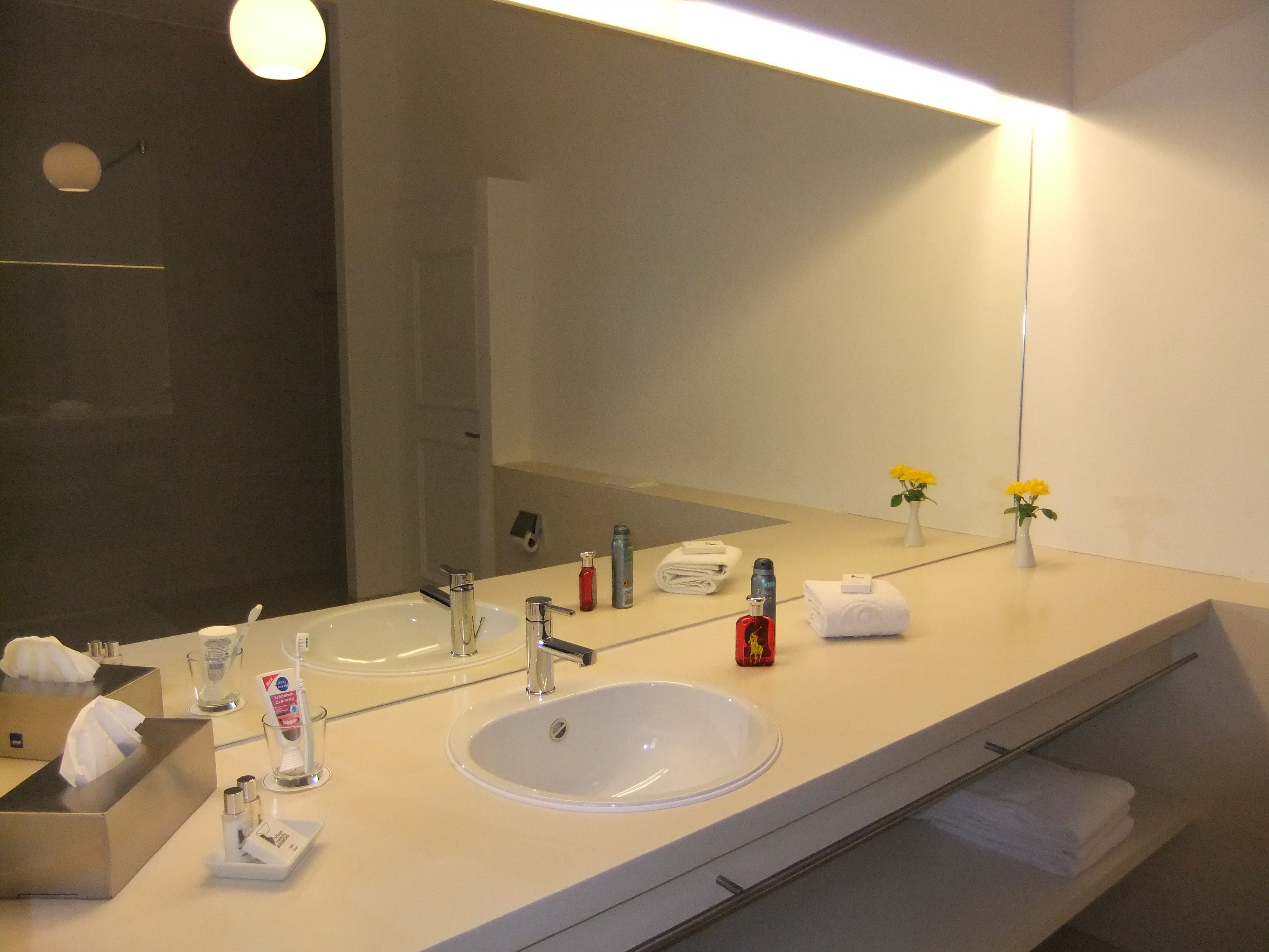 A modern bathroom with a large mirror, two sinks, and a towel rack.