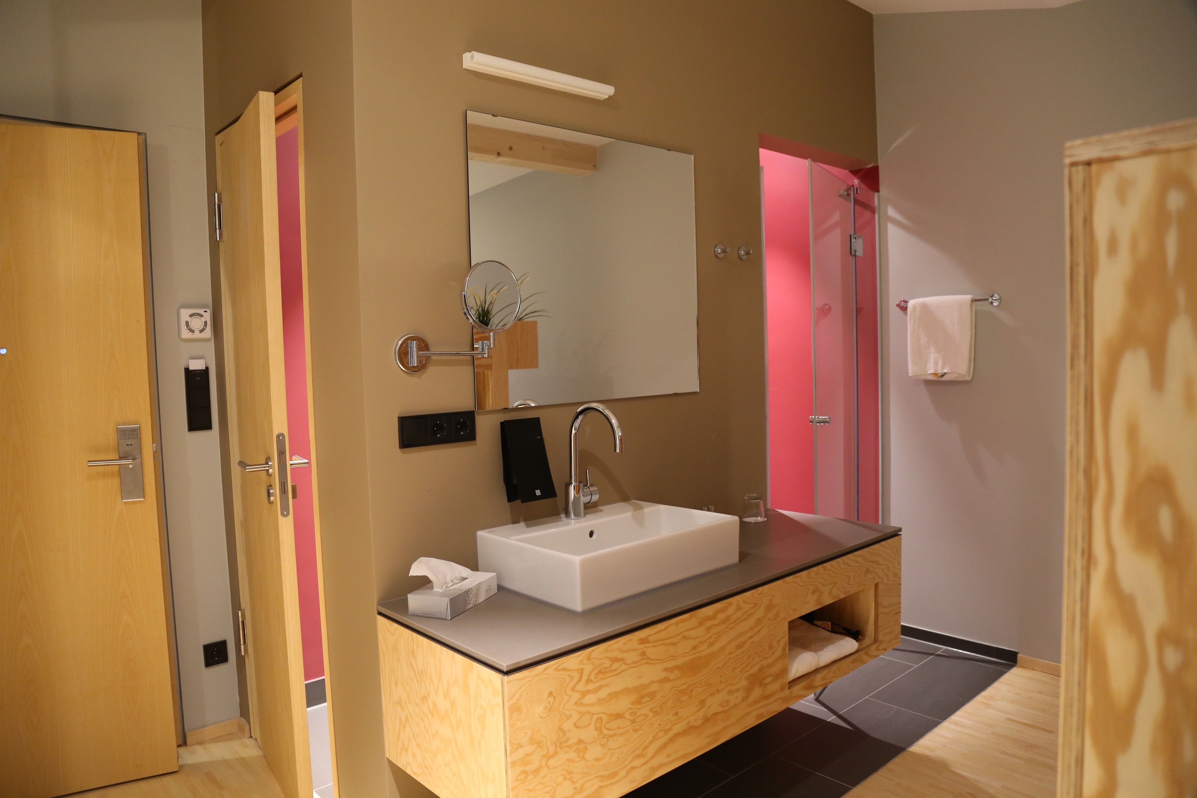 A modern bathroom with a wooden vanity, a large mirror, a white sink, and a towel rack.