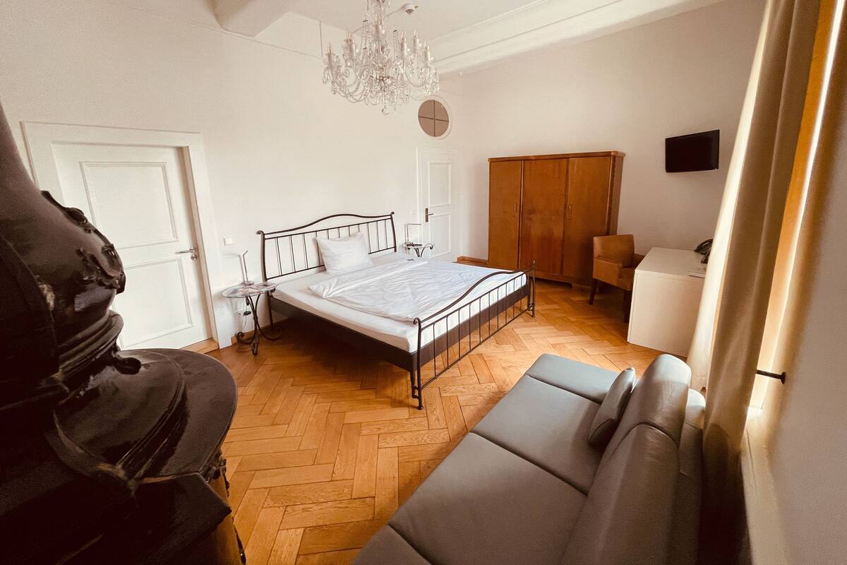 A bedroom with a bed, a wooden wardrobe, a desk, a chair, a sofa, and a chandelier.
