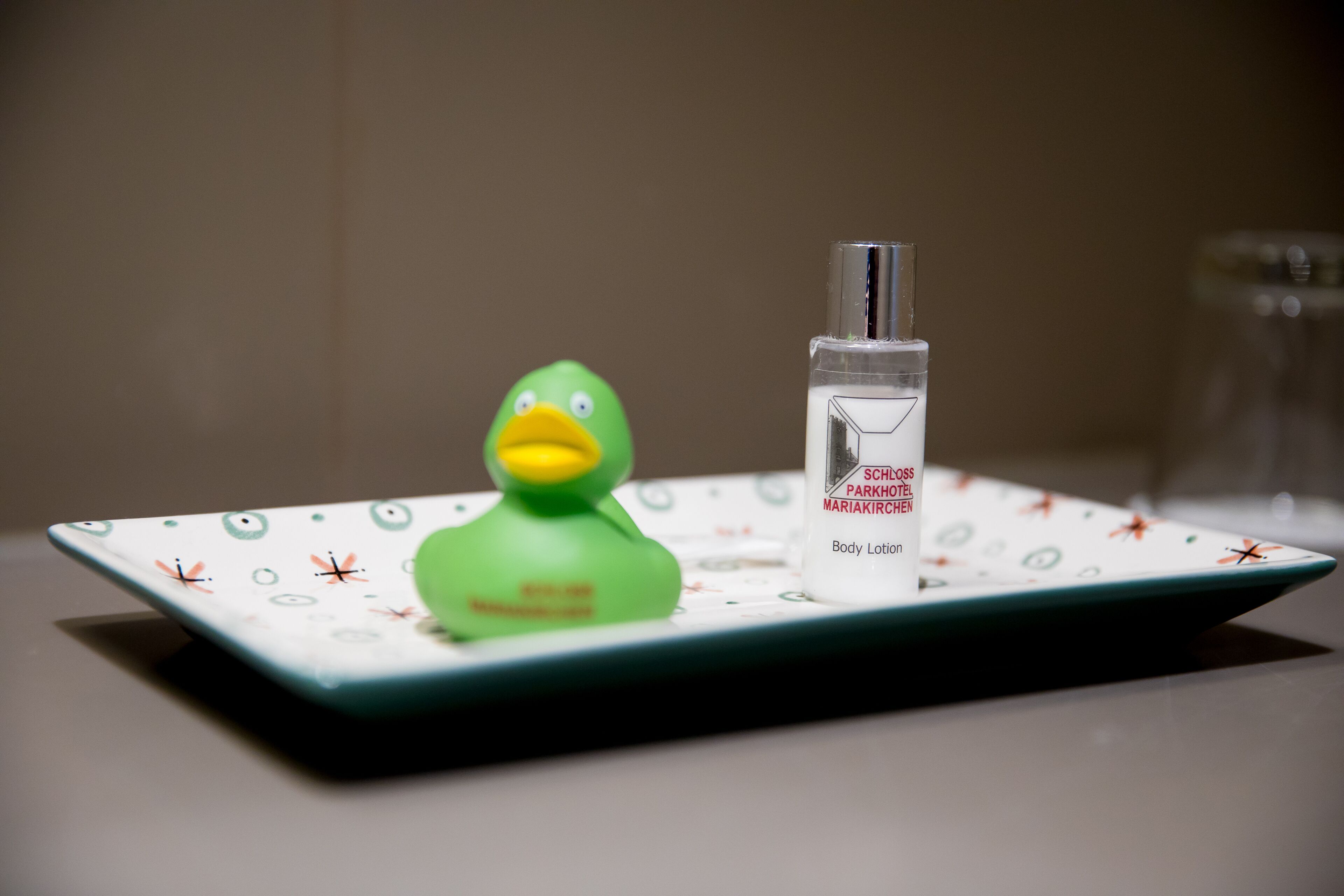 A green rubber duck on a white tray with a bottle of body lotion.